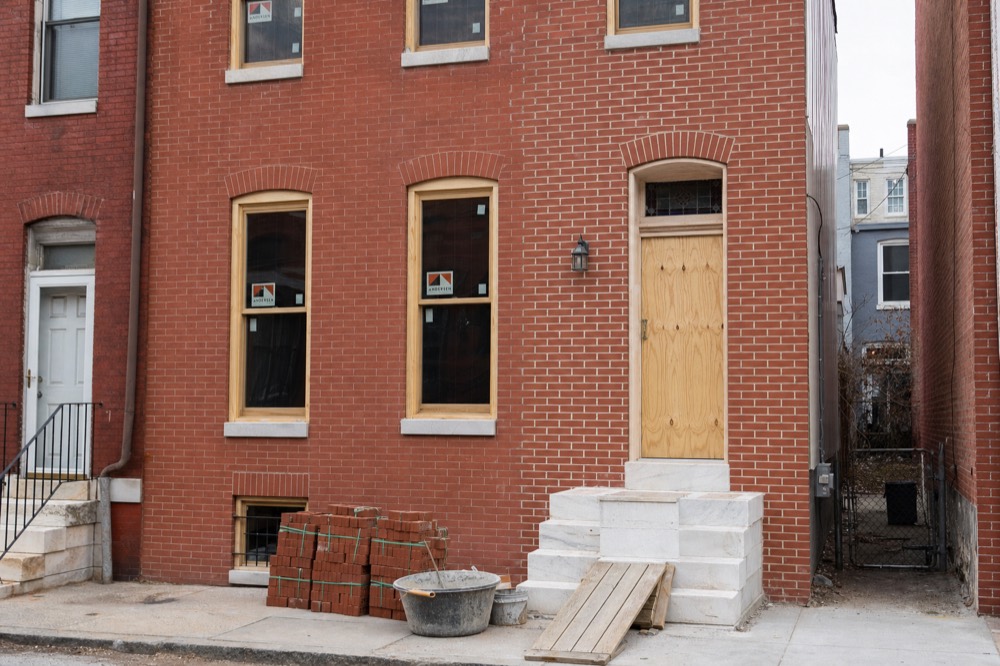 A vacant Baltimore brick rowhouse mid renovation with new window frames and repointed mortar.